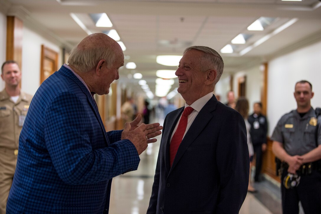 Defense Secretary James N. Mattis laughs while talking with Terry Bradshaw in a hallway.