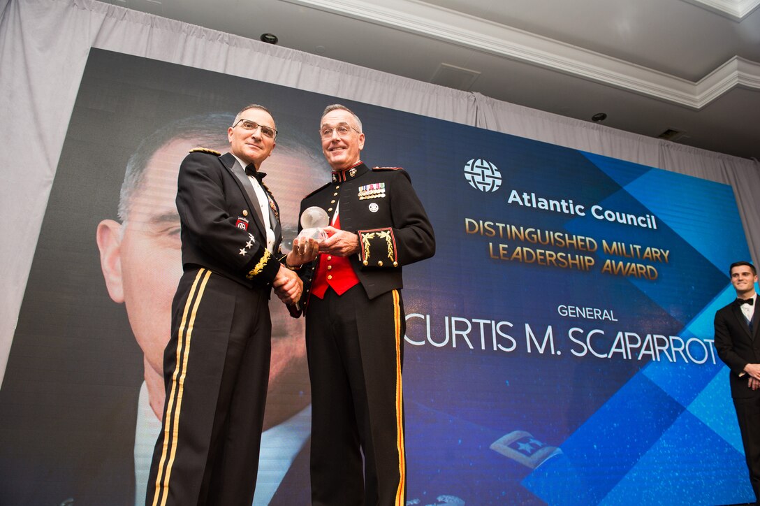 Marine Corps Gen. Joe Dunford stands and presents an award to Army Gen. Curtis M. Scaparrotti as the two shake hands.