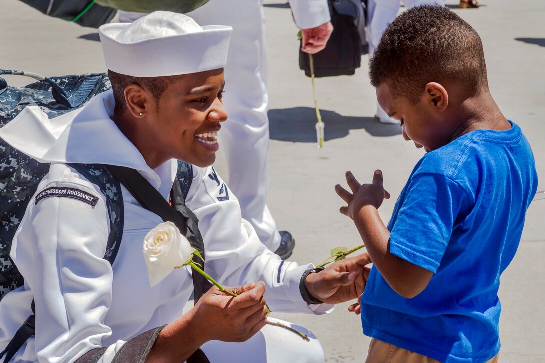 A smiling mother kneels and touches her son as he points something out to her.