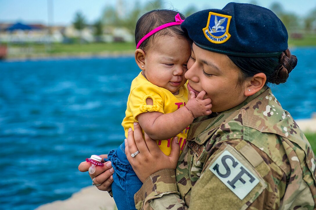 An airman holds her baby daughter, who caresses her mom's face.