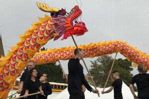 People wearing all black carry maneuver a red and orange dragon puppet held on sticks.