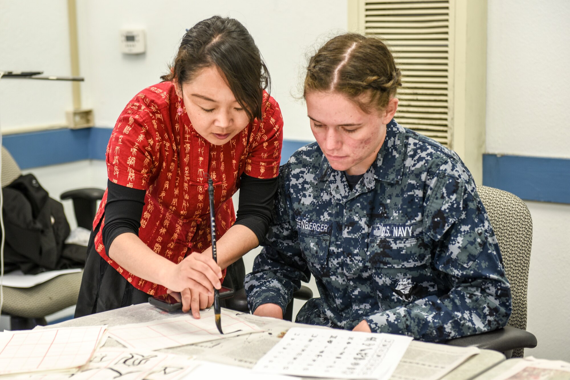 Cong Li, Defense Language Institute assistant Chinese professor, demonstrates how to write Chinese characters to Seaman Madelyn Nizenberger, Navy detachment trainee, during Defense Language Institute Foreign Language Center Language Day at the Presideo of Monterey, California, May 11, 2018. In addition to dances, music, and cultural tents, Language Day also included classroom demonstrations.
