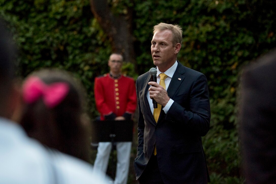 Deputy Defense Secretary Patrick M. Shanahan stands and speaks into a handheld microphone to guests outside.