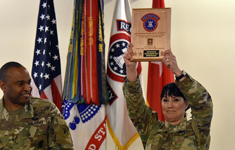 Two soldiers standing next to each other one is holding a plaque in the air above her head