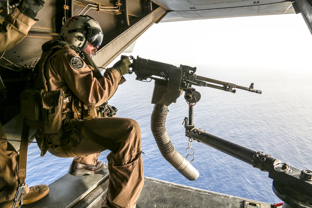 A Marine sits behind a machine gun above water.
