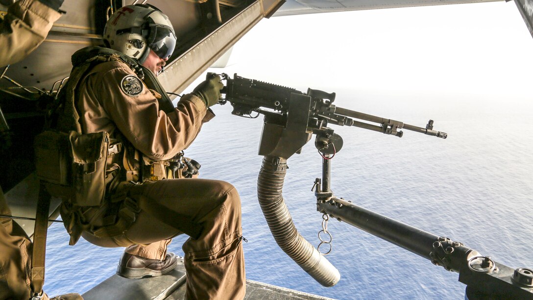 A Marine sits behind a machine gun above water.