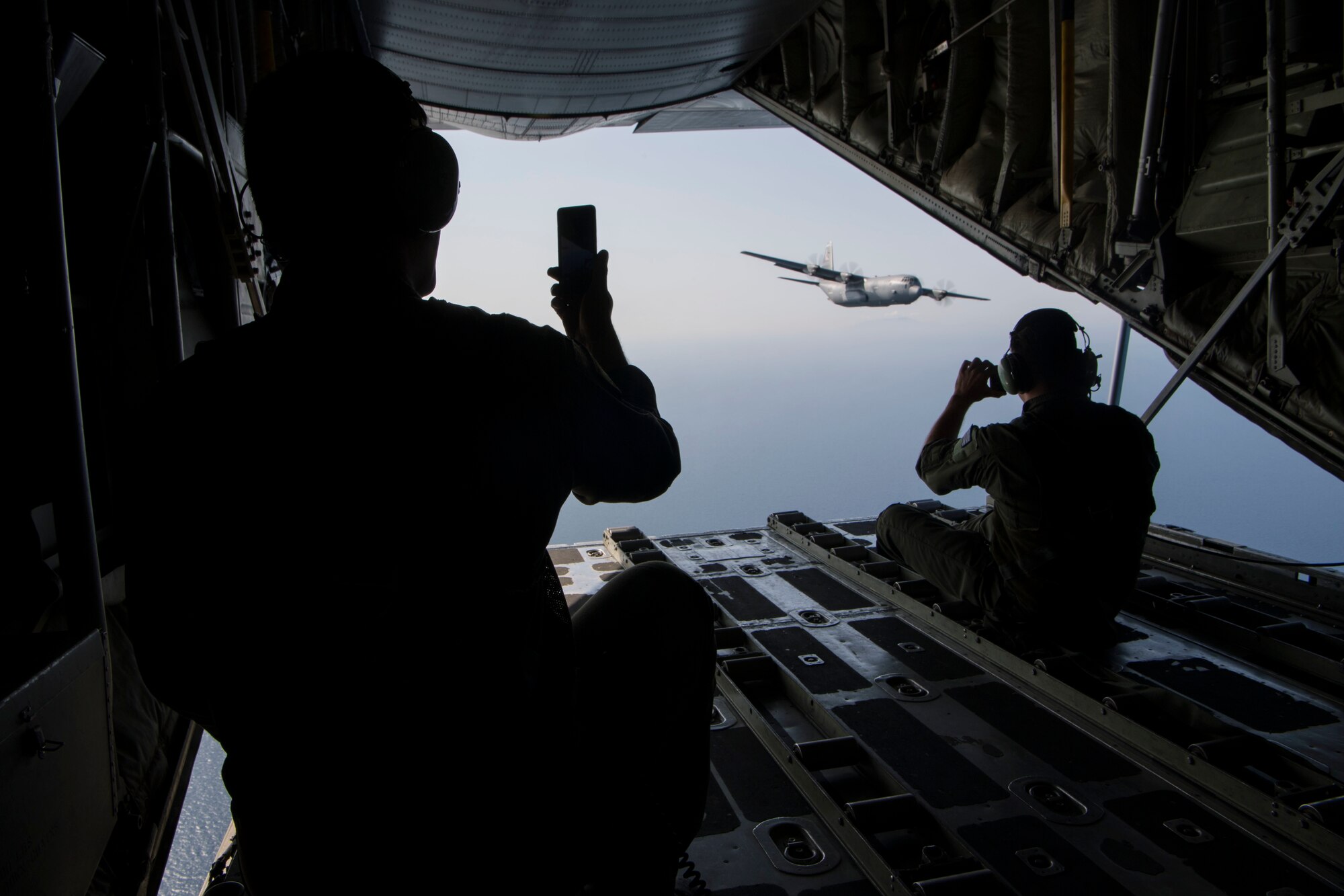 Two Hellenic air force loadmasters take photos of a U.S. Air Force C-130J Super Hercules, while riding on a Hellenic air force C-130H Hercules during an exercise Stolen Cerberus V interfly mission near Elefsis Air Base, Greece, May 10, 2018. The two aircraft flew in formation through different drop zones. (U.S. Air Force photo by Senior Airman Devin M. Rumbaugh)