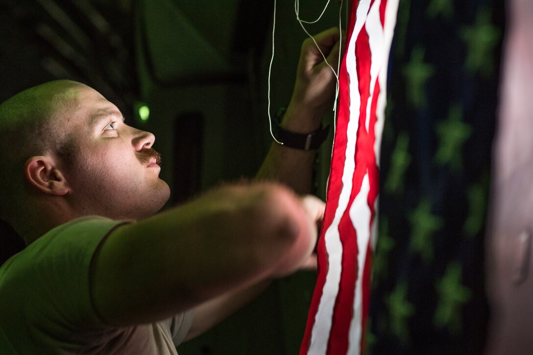 U.S. Air Force Senior Airman Jeremy Kosick, 816th Expeditionary Airlift Squadron instructor loadmaster, hangs a U.S. flag onboard a C-17 Globemaster III during a airdrop mission over Afghanistan, May 10, 2018. The C-17 transported troops and cargo to forward operating locations throughout the U.S. Central Command area of responsibility in support of Operation Freedom Sentinel mission. The C-17 is not only proficient in transporting troops and supplies, but can also perform tactical airlift and airdrop missions and transport ambulatory patients during aeromedical evacuations. (U.S. Air Force photo by Staff Sgt. Keith James)