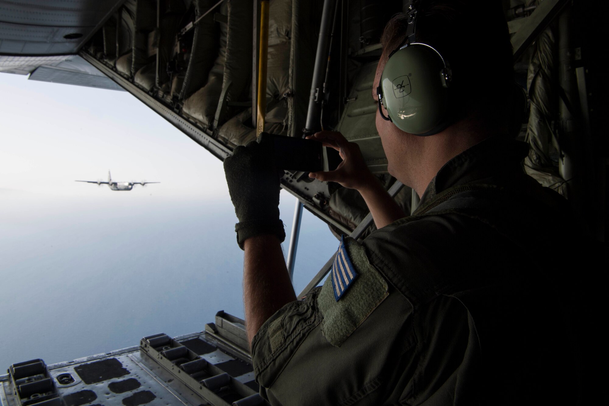 A Hellenic air force loadmaster takes photos of a U.S. Air Force C-130J Super Hercules during an exercise Stolen Cerberus V interfly mission in the skies near Elefsis Air Base, Greece, May 10, 2018. One U.S. Air Force C-130J and one Hellenic Air Force C-130H Hercules participated in the flight. (U.S. Air Force photo by Senior Airman Devin M. Rumbaugh)