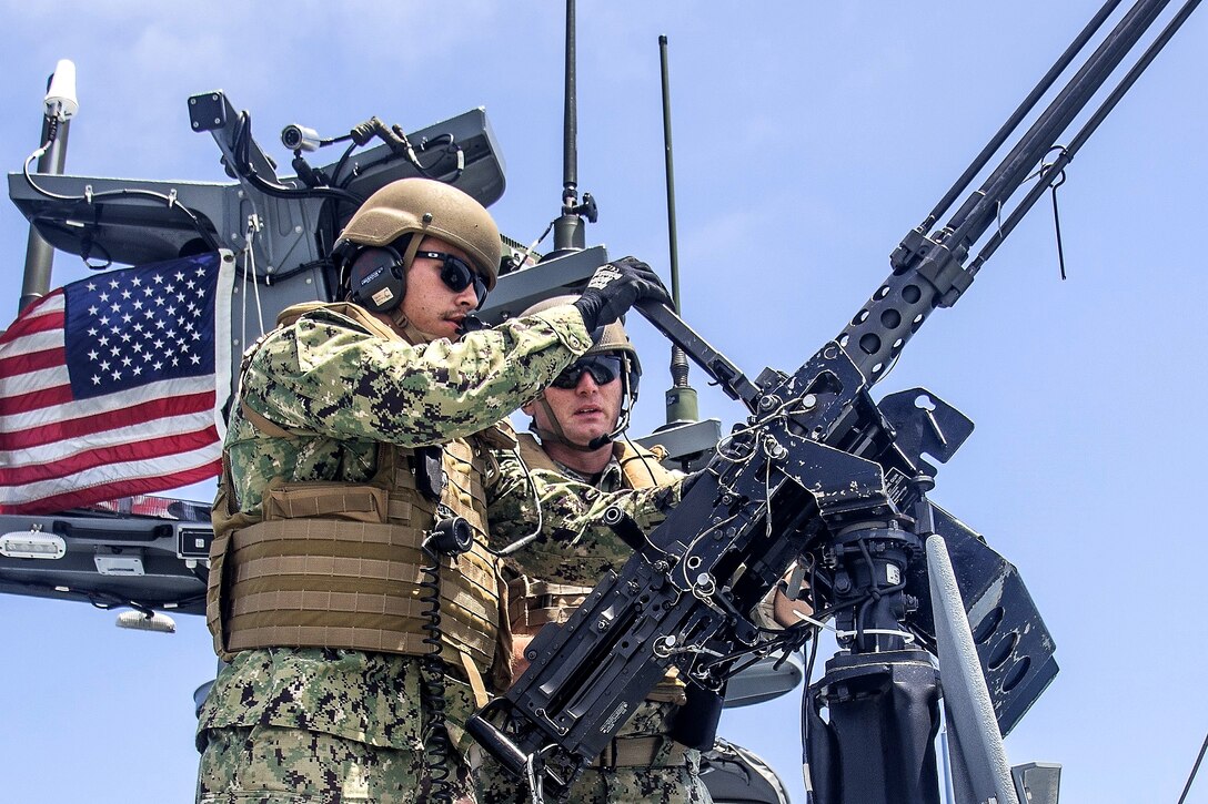 A quartermaster instructs a sailor reloading a .50-caliber machine gun.
