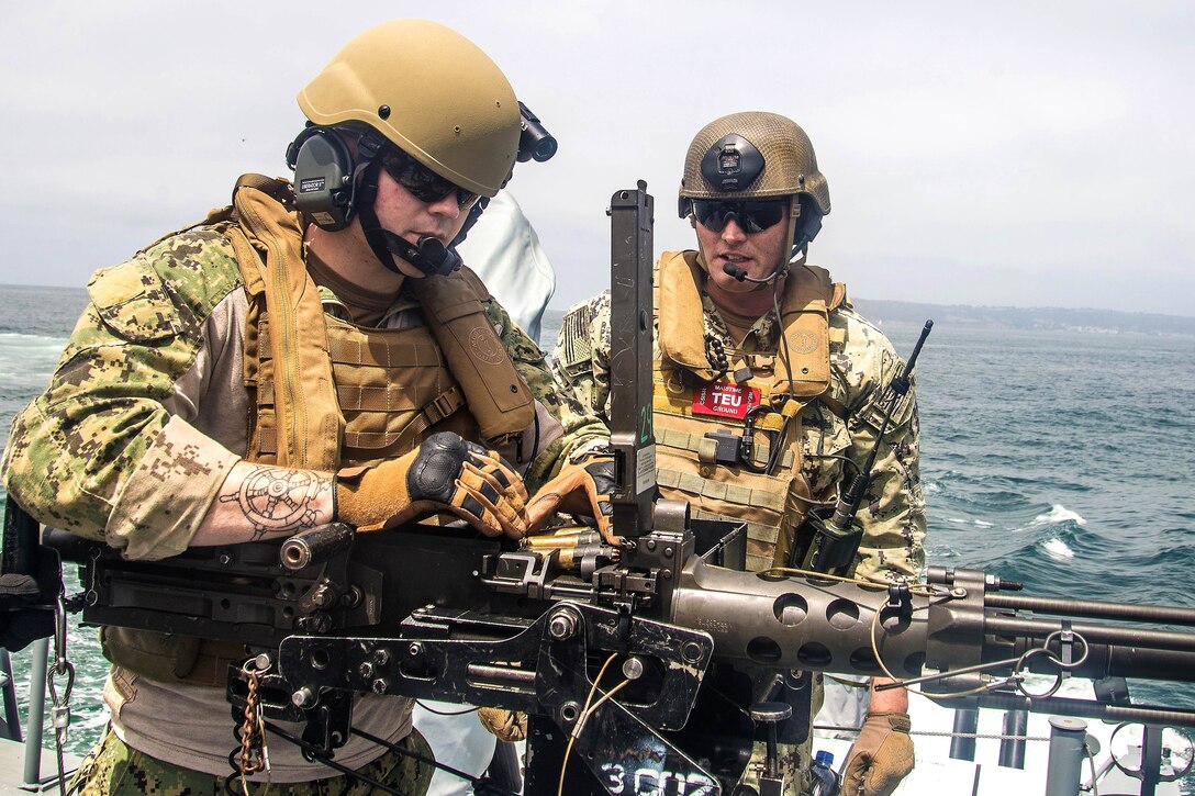 A quartermaster instructs a sailor reloading a .50-caliber machine gun.