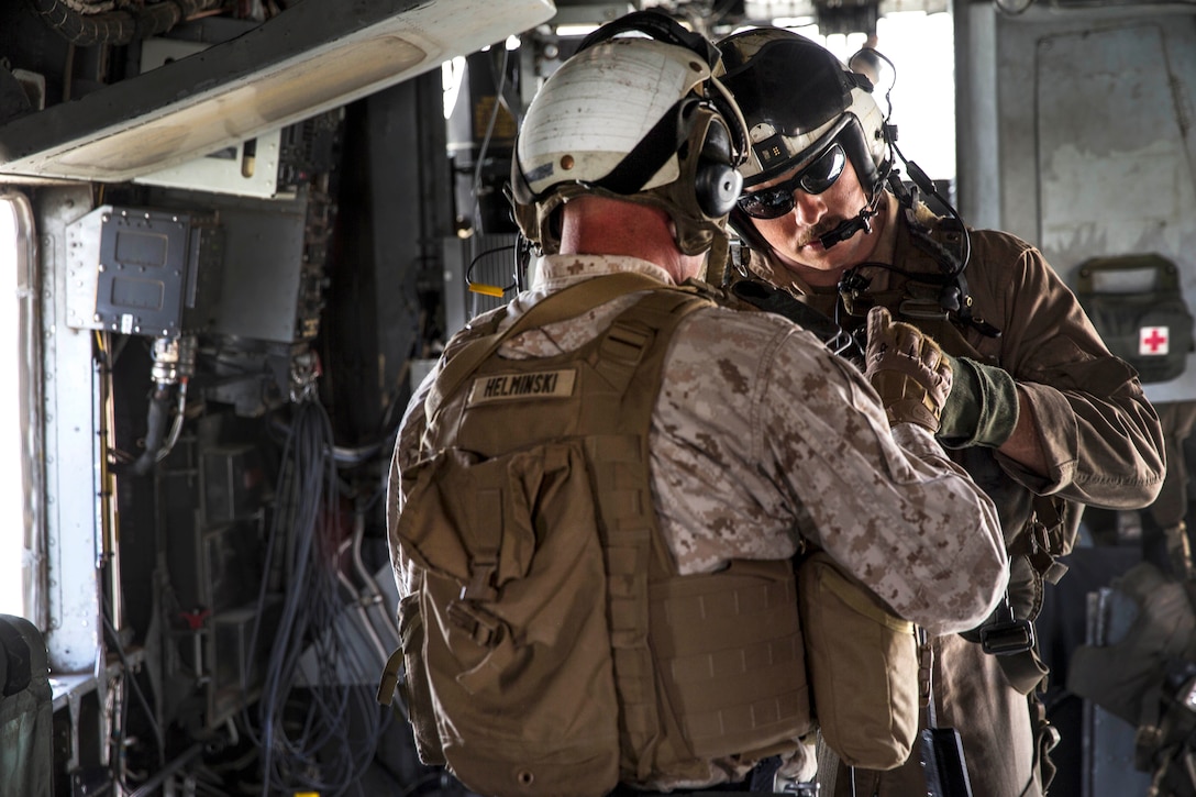 A Marine crew chief checks another Marine’s communications gear.