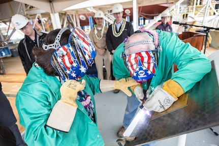 Irene Hirano Inouye (left), future USS Daniel Inouye (DDG 118) sponsor and wife of the late Sen. Daniel Inouye, and a Bath Iron Works employee etch Inouye’s initials on to the keel plate during the ship’s keel authentication ceremony in Bath, Maine, May 14.