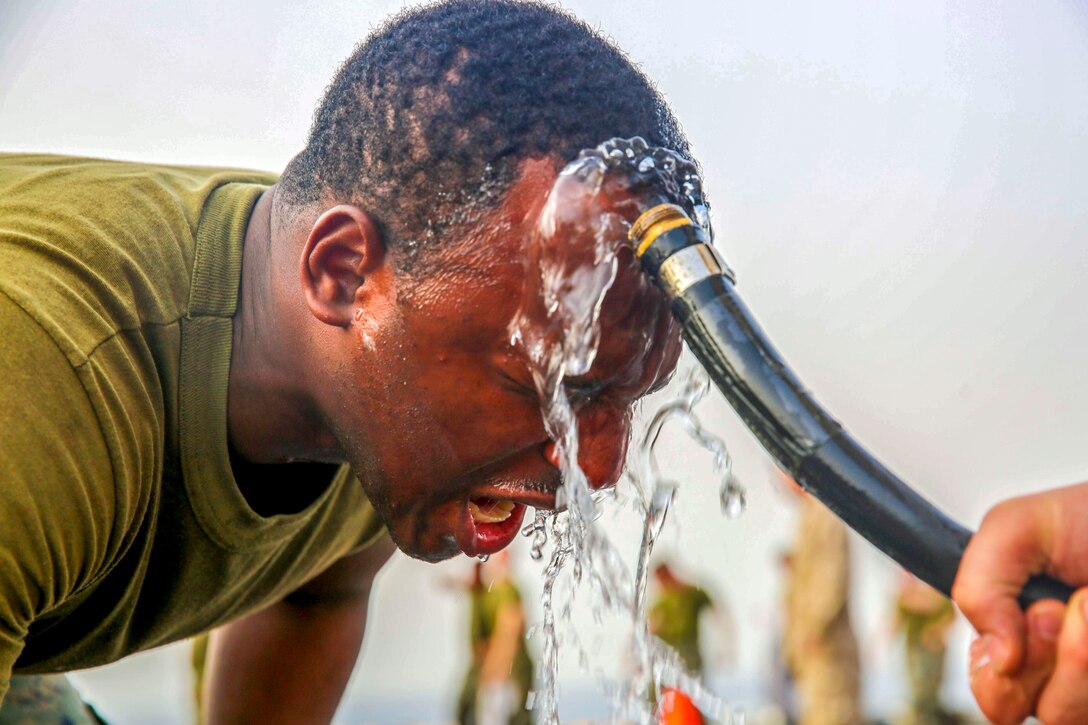 A Marine uses a hose to wash his face.