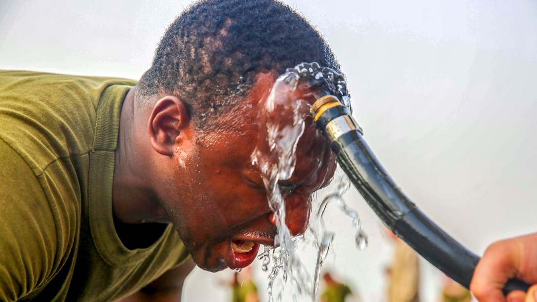 A Marine uses a hose to wash his face.
