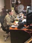U.S Army Sgt. Ann Kelnhofer, a wheeled vehicle mechanic assigned to Company E, 1st Battalion, 126th Aviation Regiment, sits alongside a fellow service member to complete mission essential tasks and prepare for the next work day at Union III Forward Operating Base.  Kelnhofer works as the Air Movement Coordinator and personnel terminal for areas of operations in Union III.