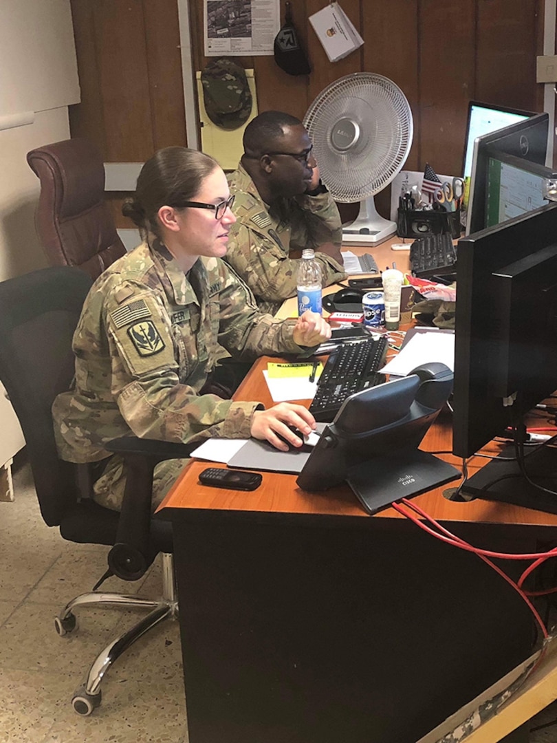 U.S Army Sgt. Ann Kelnhofer, a wheeled vehicle mechanic assigned to Company E, 1st Battalion, 126th Aviation Regiment, sits alongside a fellow service member to complete mission essential tasks and prepare for the next work day at Union III Forward Operating Base.  Kelnhofer works as the Air Movement Coordinator and personnel terminal for areas of operations in Union III.