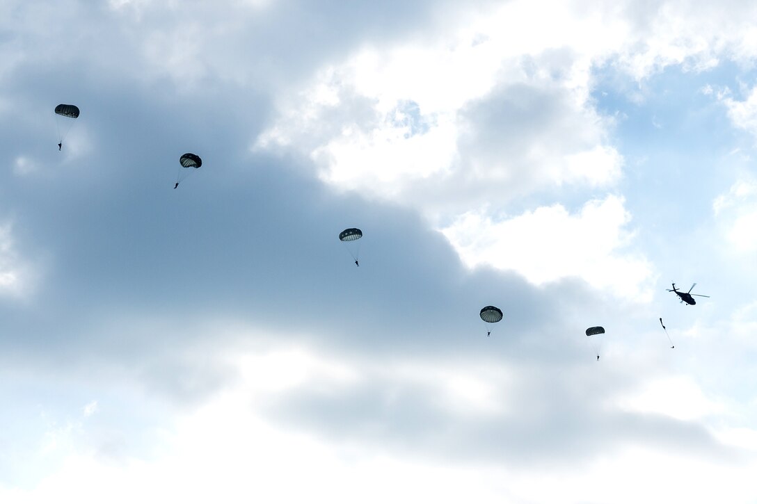 Soldiers descend from the sky after jumping out of a helicopter.