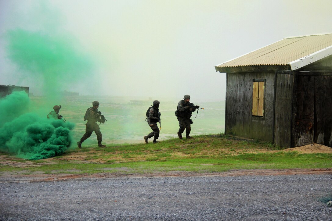 Soldiers under the cover of smoke rush to enter and search a building.