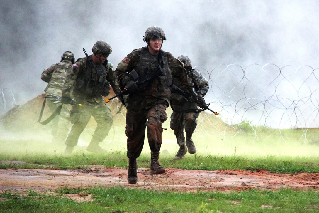 Soldiers breach a concertina obstacle under the cover of smoke.