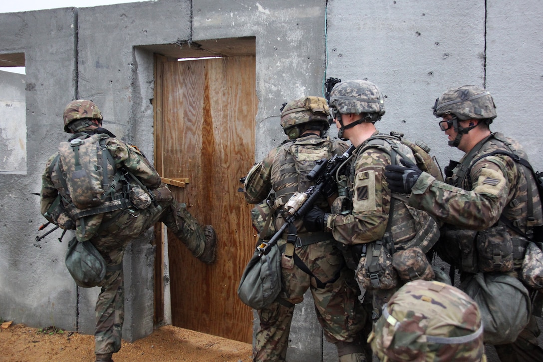 A soldier kicks in a door before his team members enter and search a building.