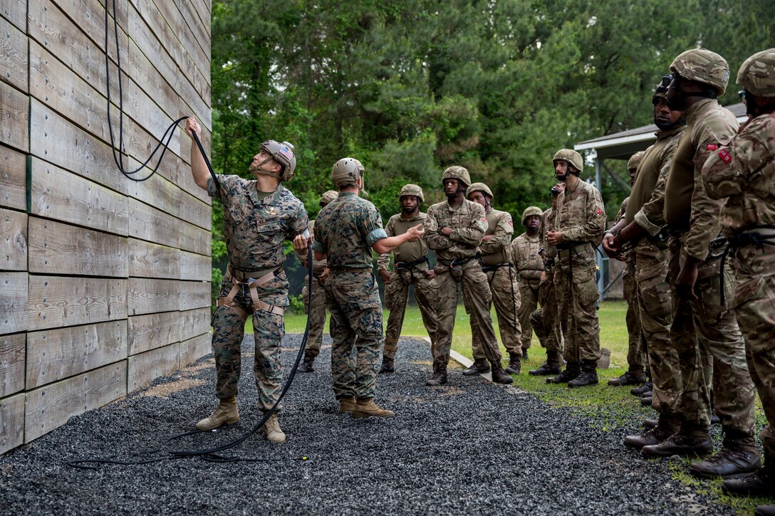 The Soldiers from the Royal Bermuda Regiment listen as Staff Sgt. Adam Powell, reconnaissance man, 2nd Reconnaissance Battalion, 2nd Marine Division, and Sgt. Johnny Senteno, reconnaissance man, 2nd Reconnaissance Battalion, 2nd Marine Division, explains how belaying will operate during their rappelling training at Stone Bay on Marine Corps Base Camp Lejeune on May 8, 2018. The regiment was at MCB Camp Lejeune for a two week evolution, the Junior Noncommissioned Officer Cadre, which is a course for promotion for the Soldiers in the regiment and is open to all Soldiers who have completed one year of service and have the recommendation of their company commander. (U.S. Marine Corps photo by Lance Cpl. Dominique Fisk)