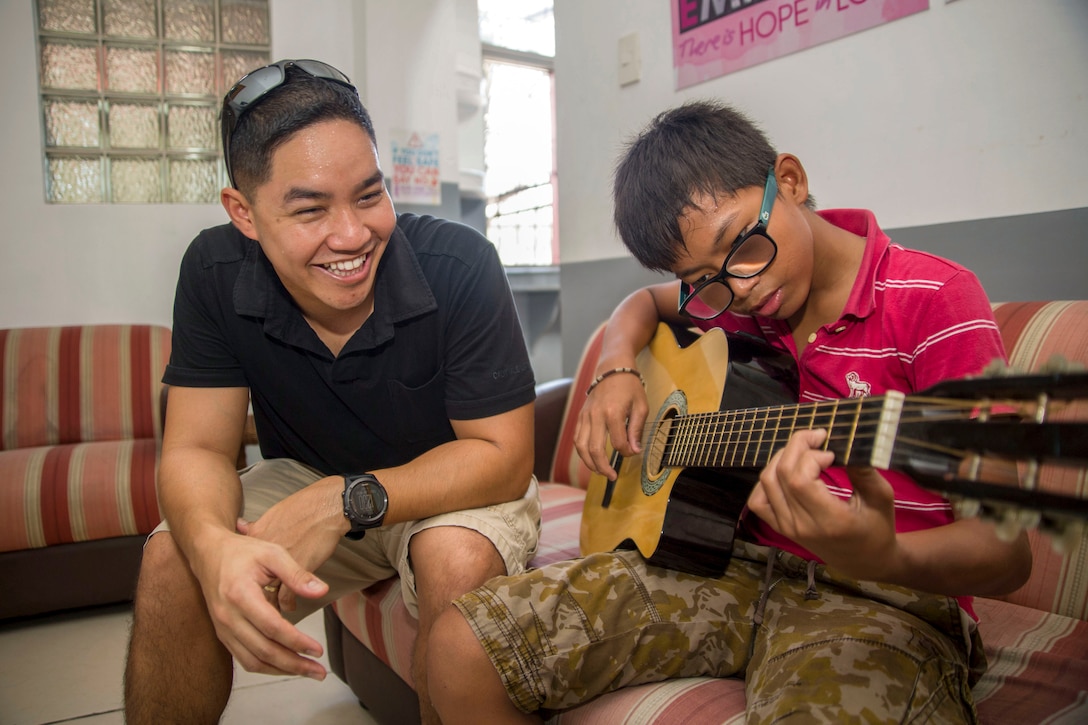 A Marine observes a child playing a guitar.