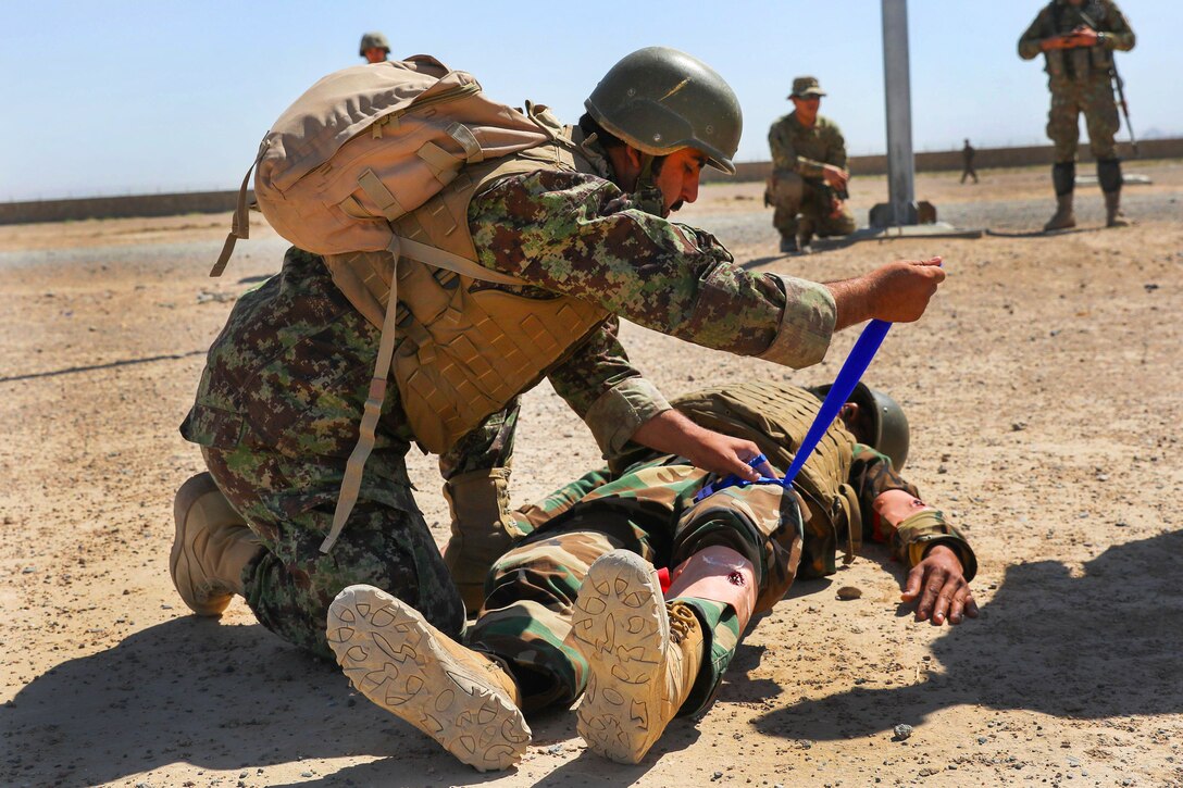 U.S. soldiers observe an Afghan soldier placing a tourniquet on a role-playing casualty.