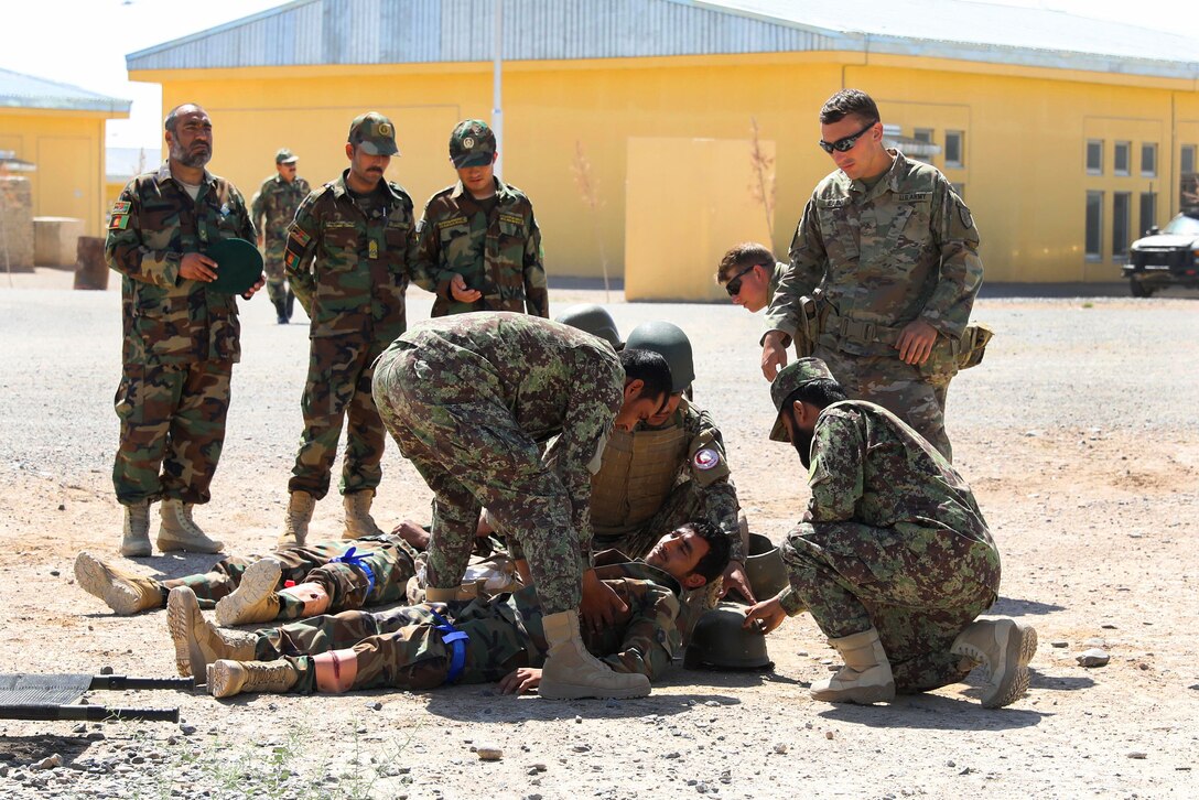 A U.S. soldier observes Afghan soldiers providing medical aid.