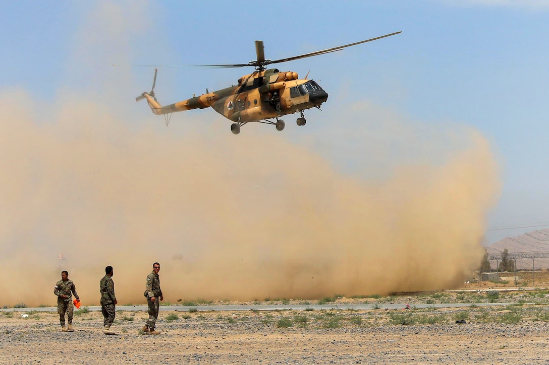 A U.S. soldier and Afghan soldiers wait for an Mi-17 helicopter to land.