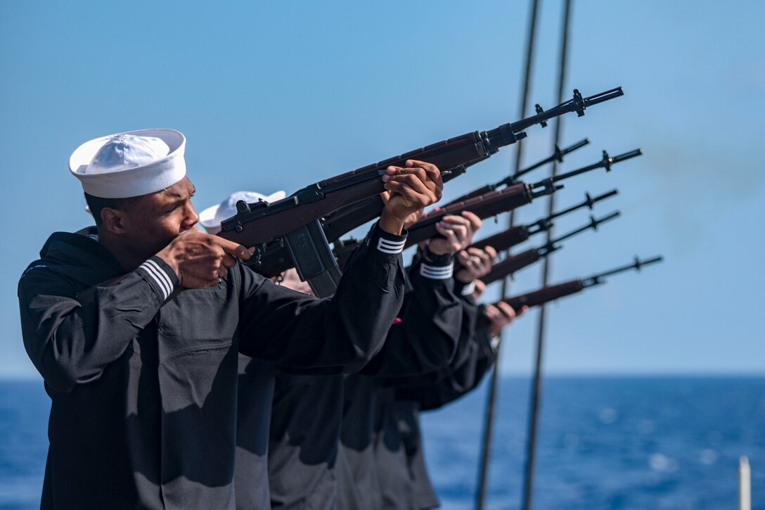 Sailors participate in a firing squad during a burial-at-sea.