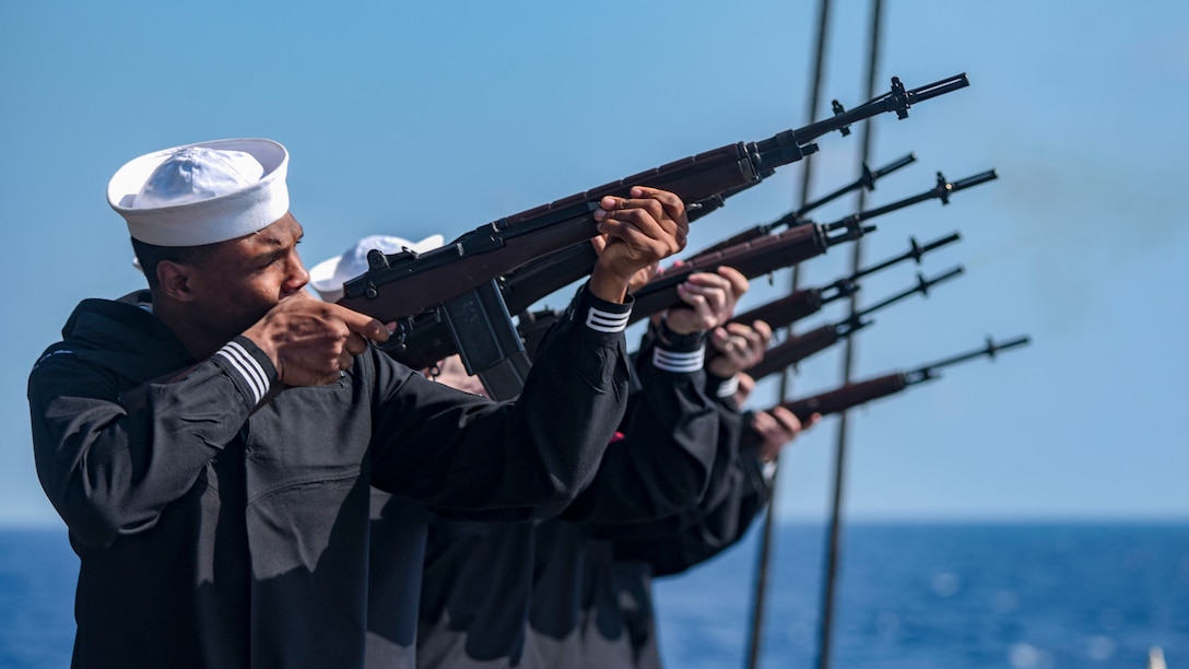 Sailors participate in a firing squad during a burial-at-sea.