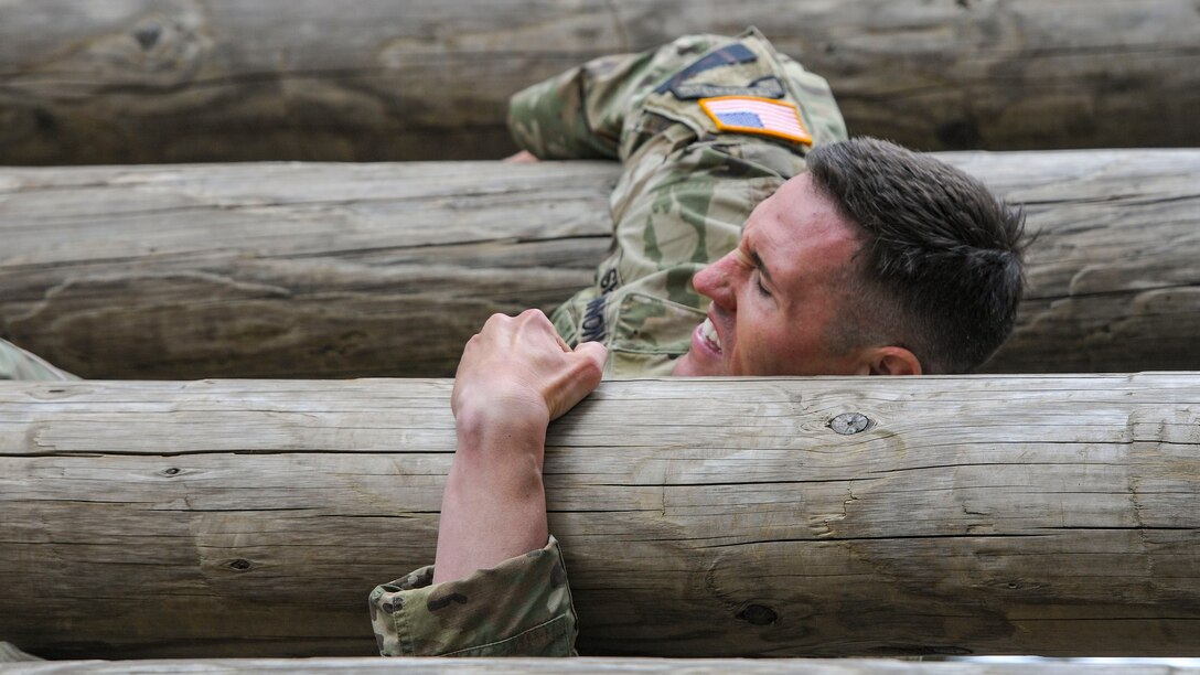 A soldier holds himself up on an obstacle course.