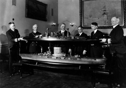 Rear Adm. David W. Taylor (left), chief of the Bureau of Construction and Repair, and Rear Adm. John K. Robinson (right), chief of the Bureau of Engineering, hold a model of the battle cruisers (CC-1 class) then under construction, March 8, 1922. In the foreground is a model of an aircraft carrier design converted from the battle cruiser hull. This photo illustrates the genesis of the Lexington (CV-2) class aircraft carrier design. Standing in the background are (from left to right): Rear Admiral William A. Moffett, chief of the Bureau of Aeronautics; Congressman Frederick C. Hicks of New York; Congressman Clark Burdick of Rhode Island; and Congressman Philip D. Swing of California. (Photographed at the Navy Department by Harris & Ewing. Photograph from Department of the Navy collections in the U.S. National Archives " 80-CF-385b)