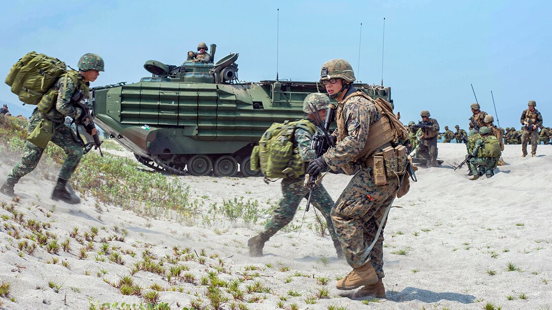 U.S. and Philippine service members run on the beach near heavy equipment.