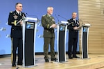Three people stand on a stage behind podiums.