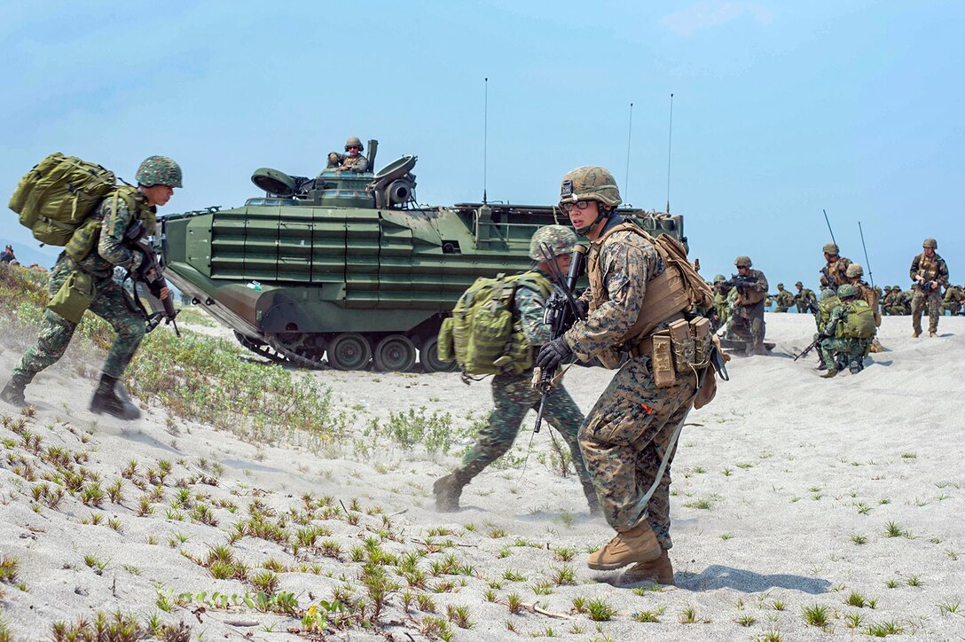 U.S. and Philippine service members run on the beach near heavy equipment.