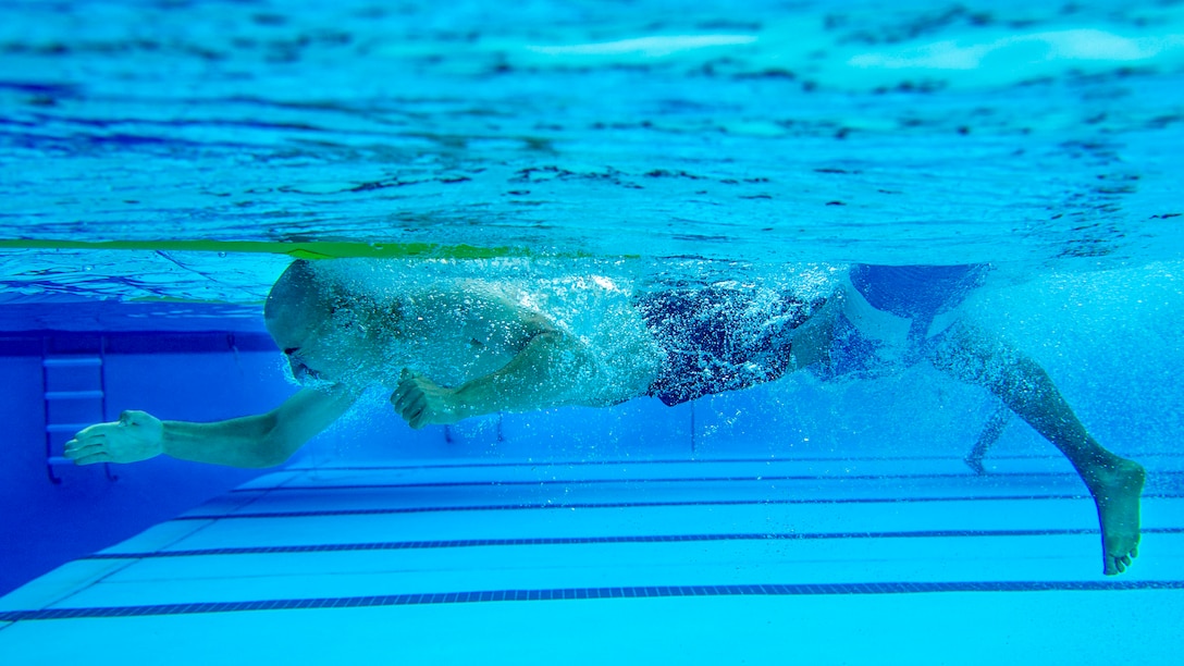 A Marine, shown in profile, reaches forward underwater while swimming in a pool.