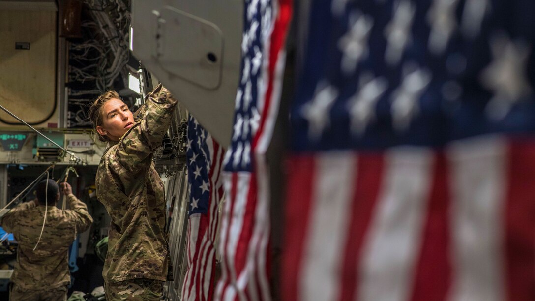 An airman hangs U.S. flags inside an aircraft.