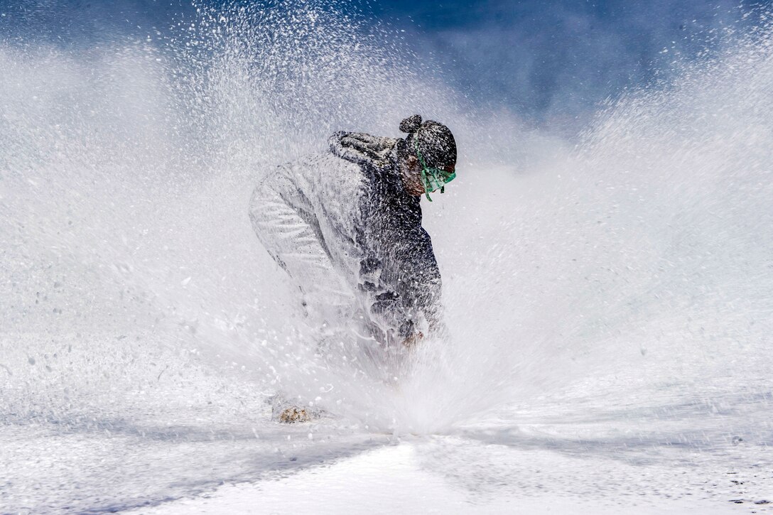 A sailor bends over a sprinkler on a flight deck, as white foam covers her and the deck, and flies up all around her.