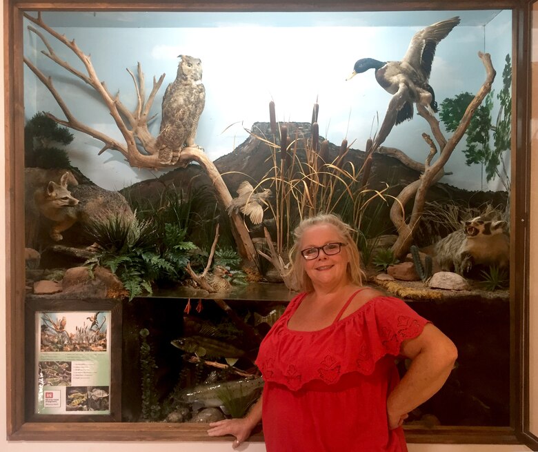 Janice Ducrepont stands in front of the visitor center’s wildlife display, May 8, 2018. She volunteered her painting skills to paint the scenic background in the display.