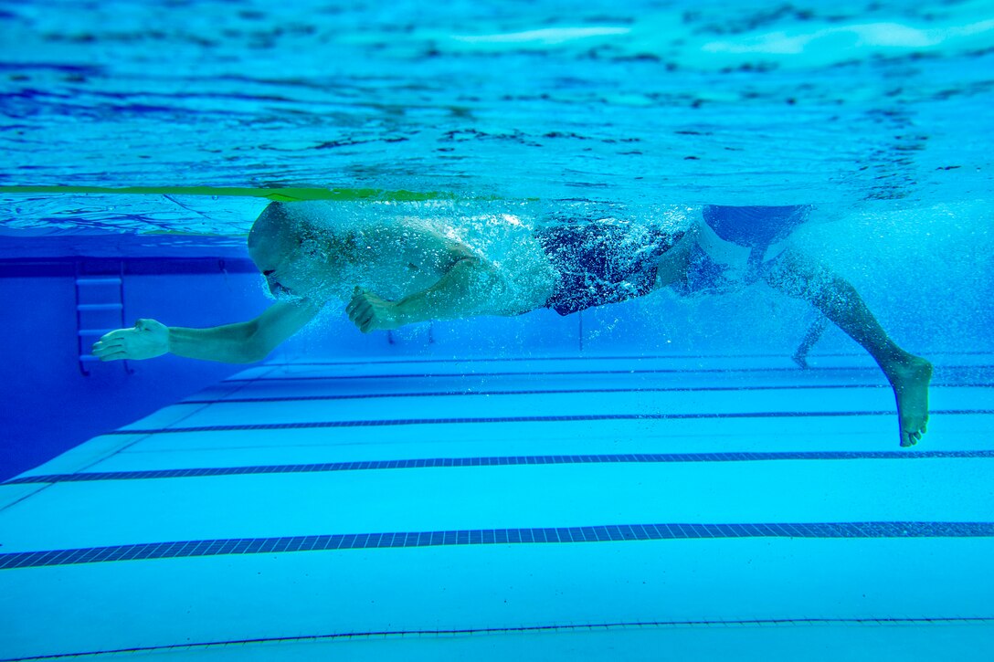 A Marine, shown in profile, reaches forward underwater while swimming in a pool.