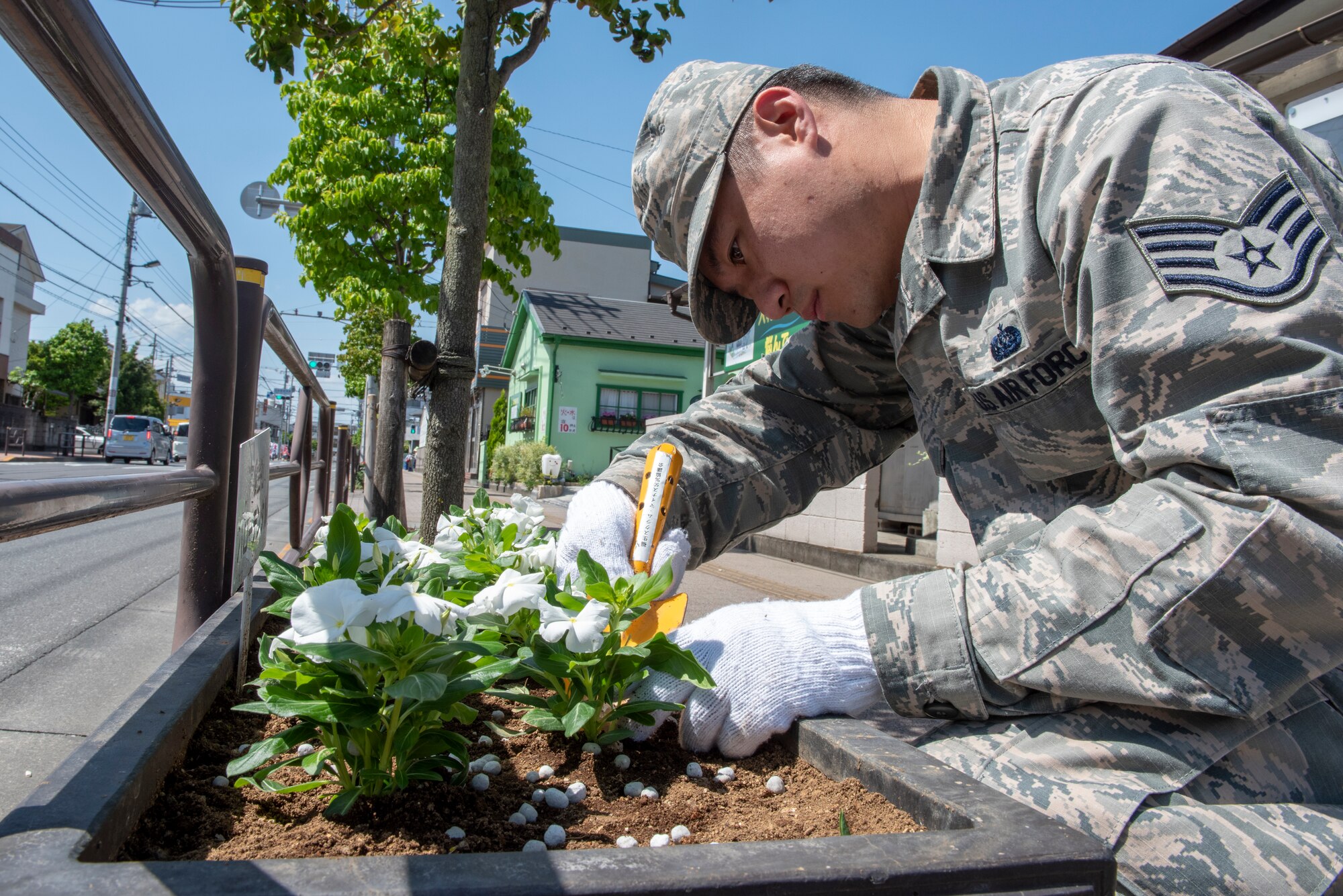 Staff Sgt. Justin Minimo, 374th Communications Squadron Operations Flight client systems technician craftsman, secures the soil around a flower during the Fussa Beautification Project just outside of Yokota Air Base in Fussa, Japan, May 14, 2018.