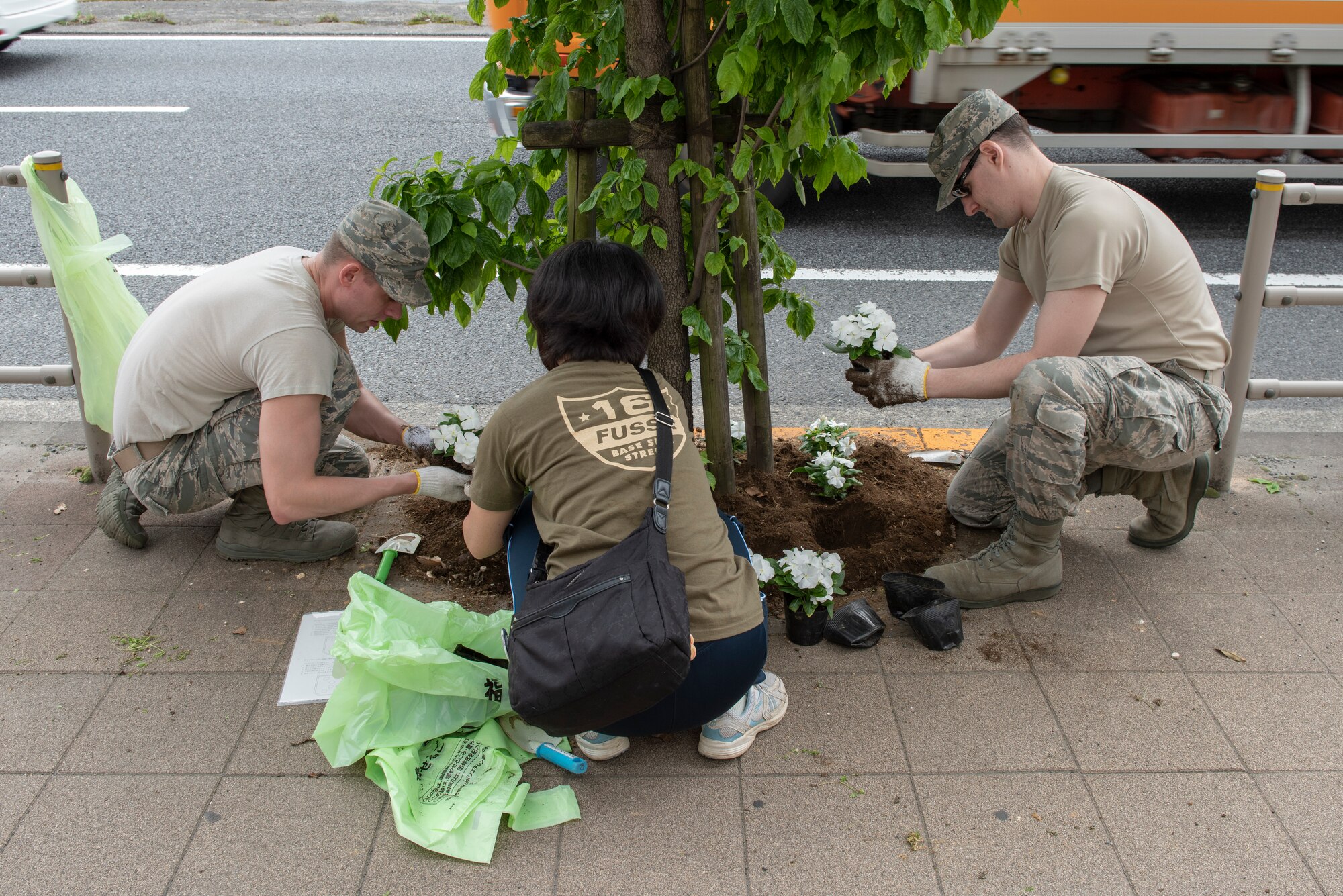 Senior Airman Patrick Heffron, 374th Communications Squadron Operations Flight client systems technician journeyman, left, and Staff Sgt. Matthew Whitton, 374 CS OF client systems technician craftsman, right, team up with a  volunteer from the local community to plant flowers for the Fussa Beautification Project outside of Yokota Air Base, Japan in Fussa May 17, 2018.