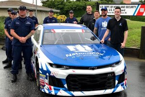 A group of men pose for a picture standing around a race car.