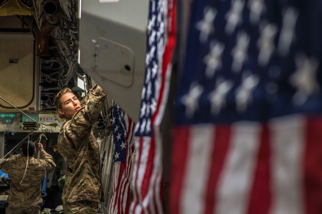 Senior Airmen Christa Stankovic, 816th Expeditionary Airlift Squadron, hangs U.S. flags onboard a C-17 Globemaster III during an airdrop mission over Afghanistan, May 10, 2018. The primary mission of the C-17 is to provide rapid strategic delivery of troops and various types of cargo to bases throughout the U.S. Central Command area of responsibility. (U.S. Air Force photo by Staff Sgt. Keith James)