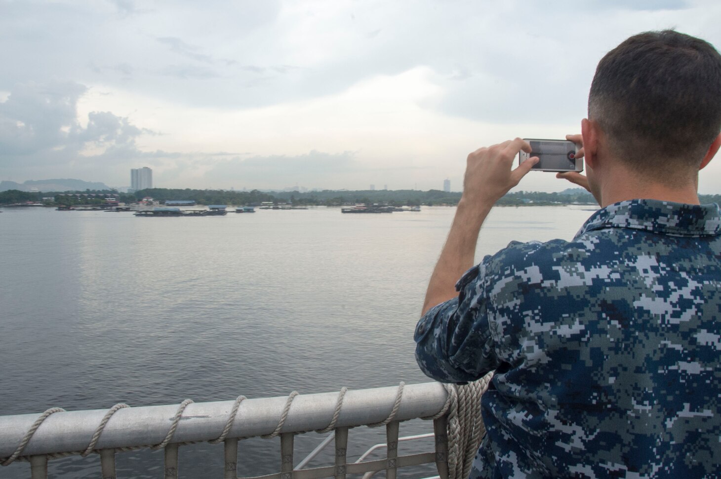 Musician 3rd Class Victor Martinez takes a picture as USNS Millinocket (T-EPF 3) departs Singapore. USNS Millinocket is supporting a U.S. 7th Fleet theater security cooperation mission and will be traveling to several Indo-Pacific countries in the coming weeks.