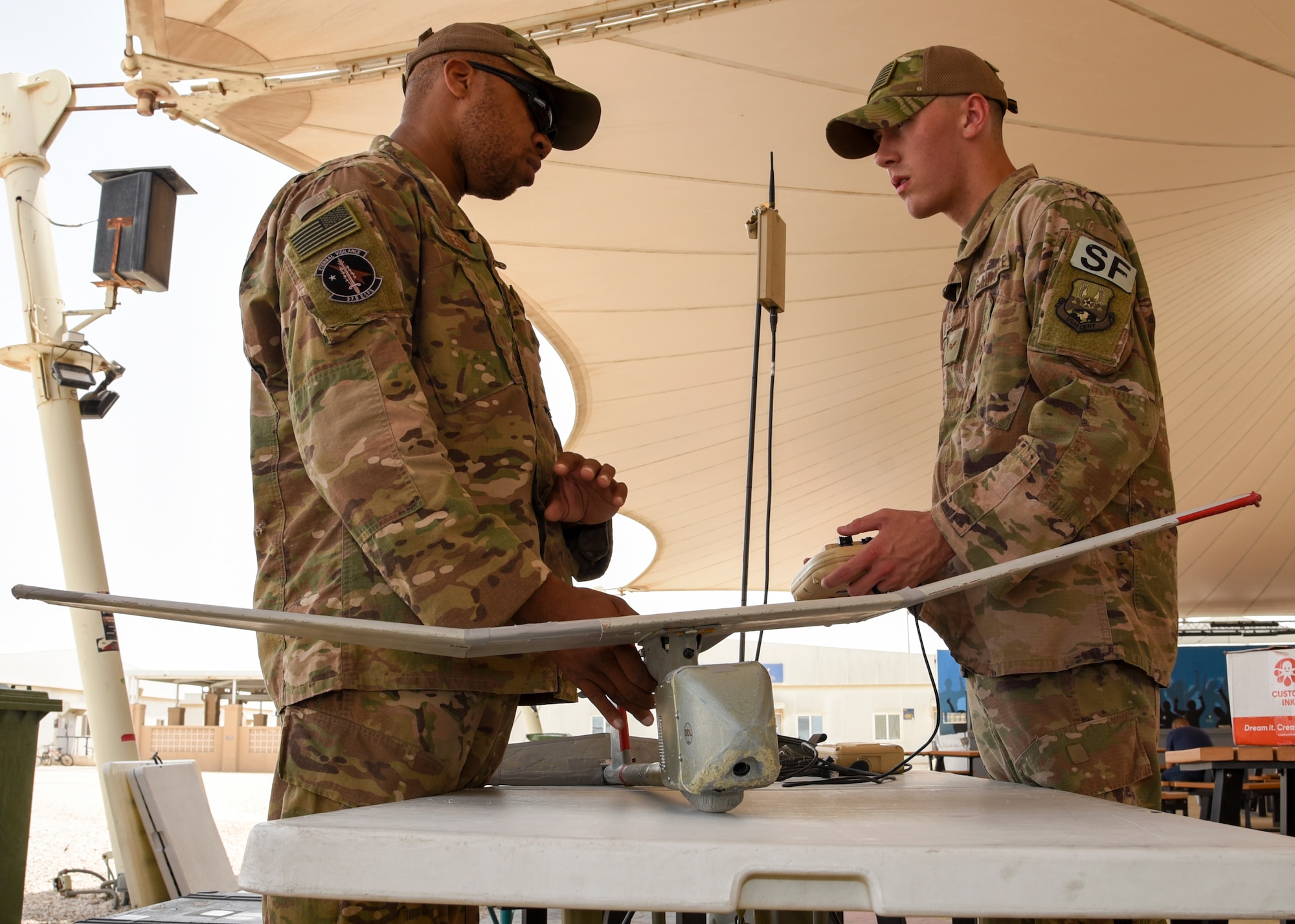 Staff Sgt. Paul Frieson (left), member of the 379th Expeditionary Security Forces Squadron, explains the capabilities of an RQ-11B, a small unmanned aircraft system, during National Police Week at Al Udeid Air Base, Qatar, May 16, 2018. The RQ-11B provides a live video feed and supports force protection efforts. (U.S. Air Force photo by Staff Sgt. Enjoli Saunders)