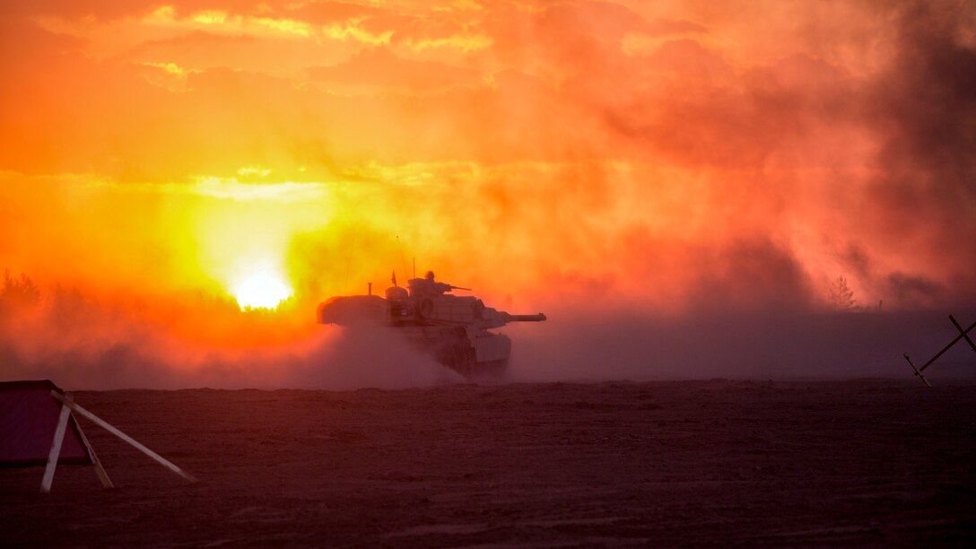A tank kicks up sand while driving on a field, illuminated by orange sky.