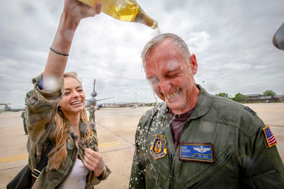 A girl pours cider from a bottle over an airman's head on a flightline.